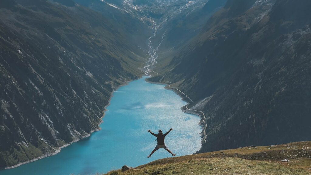 man in nature jumping for joy in front of a scenic backdrop after letting go of stress
