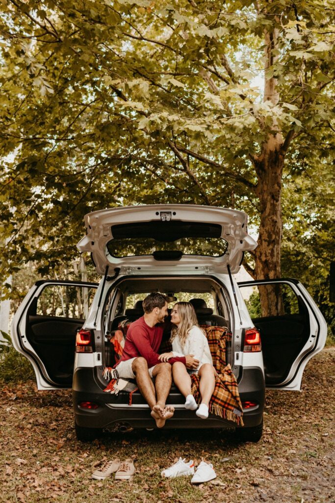 A couple sits in the trunk of an open car, staring into each other's and holding hands.