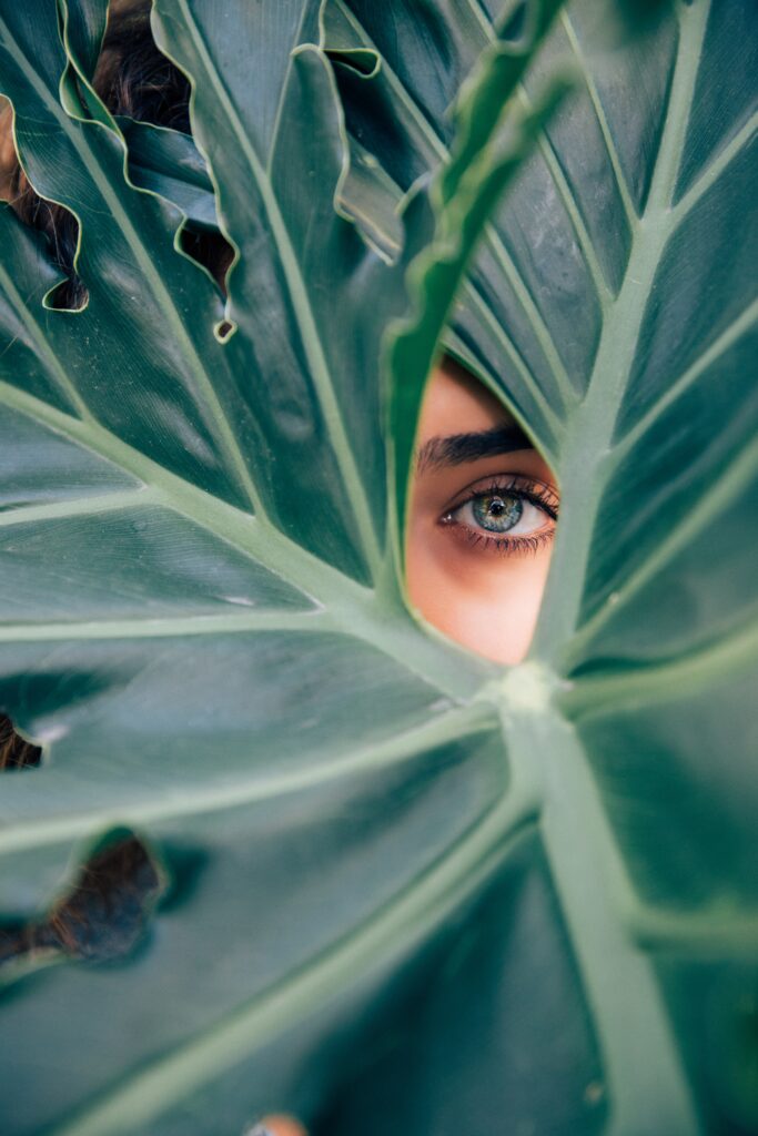 woman looking through a leaf as she ponders the mind body holistic connection