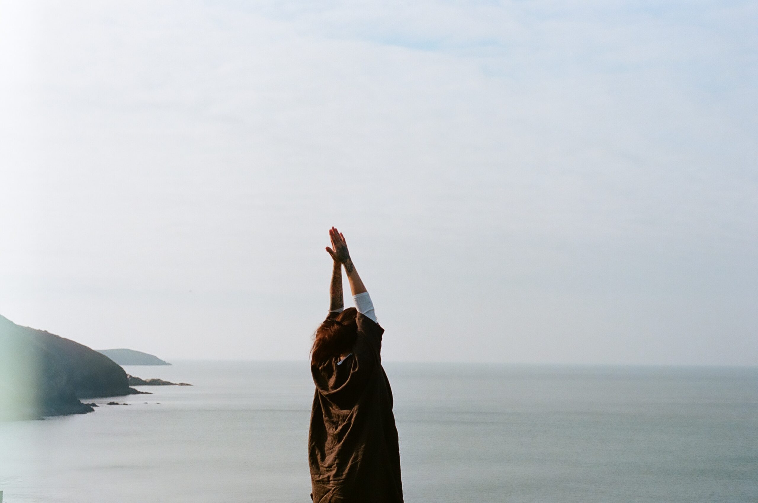 woman with her arms raised in meditation on a cloudy beach