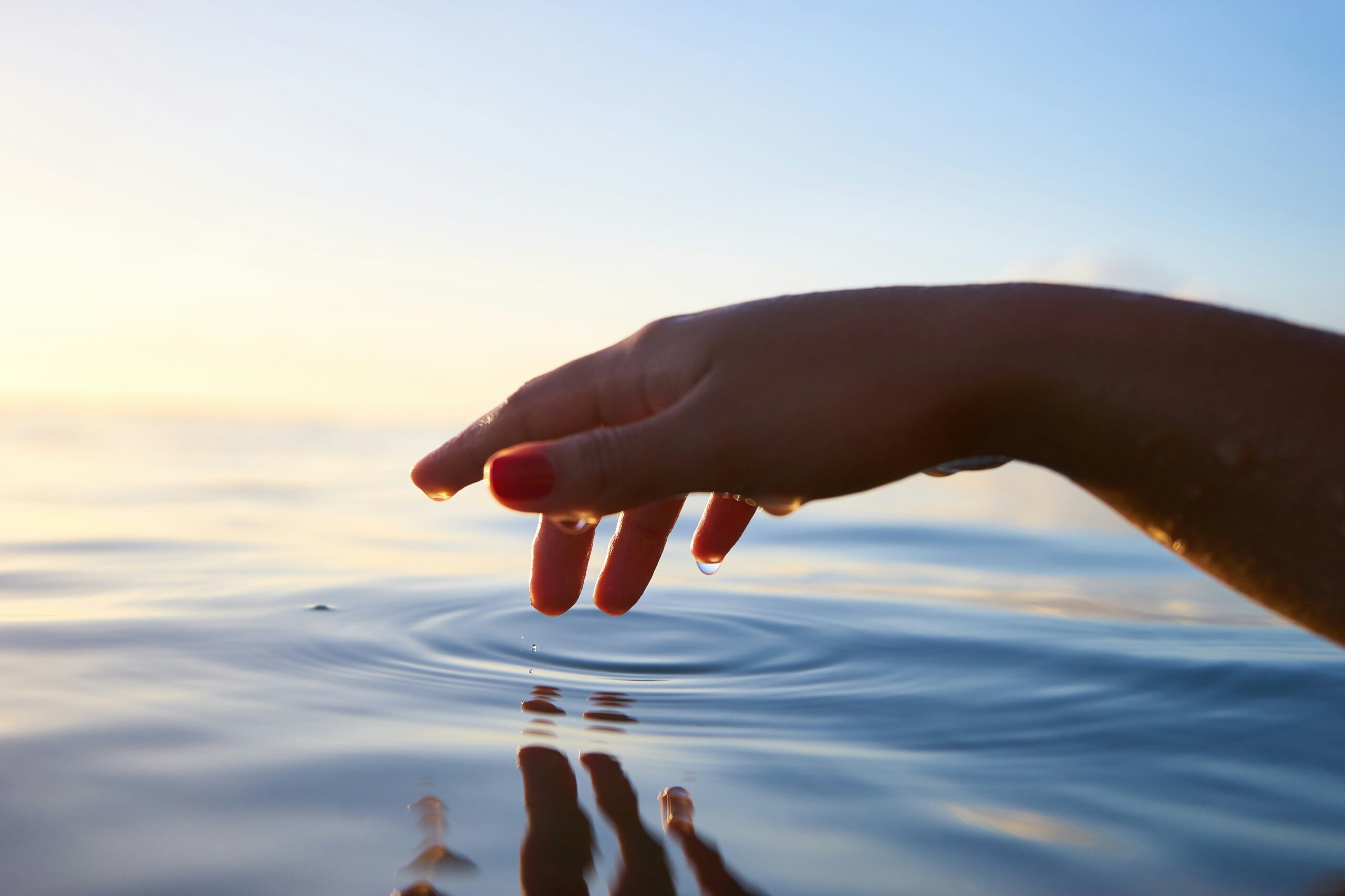 hand reaching out and touching ocean water, causing a ripple effect, in meditation