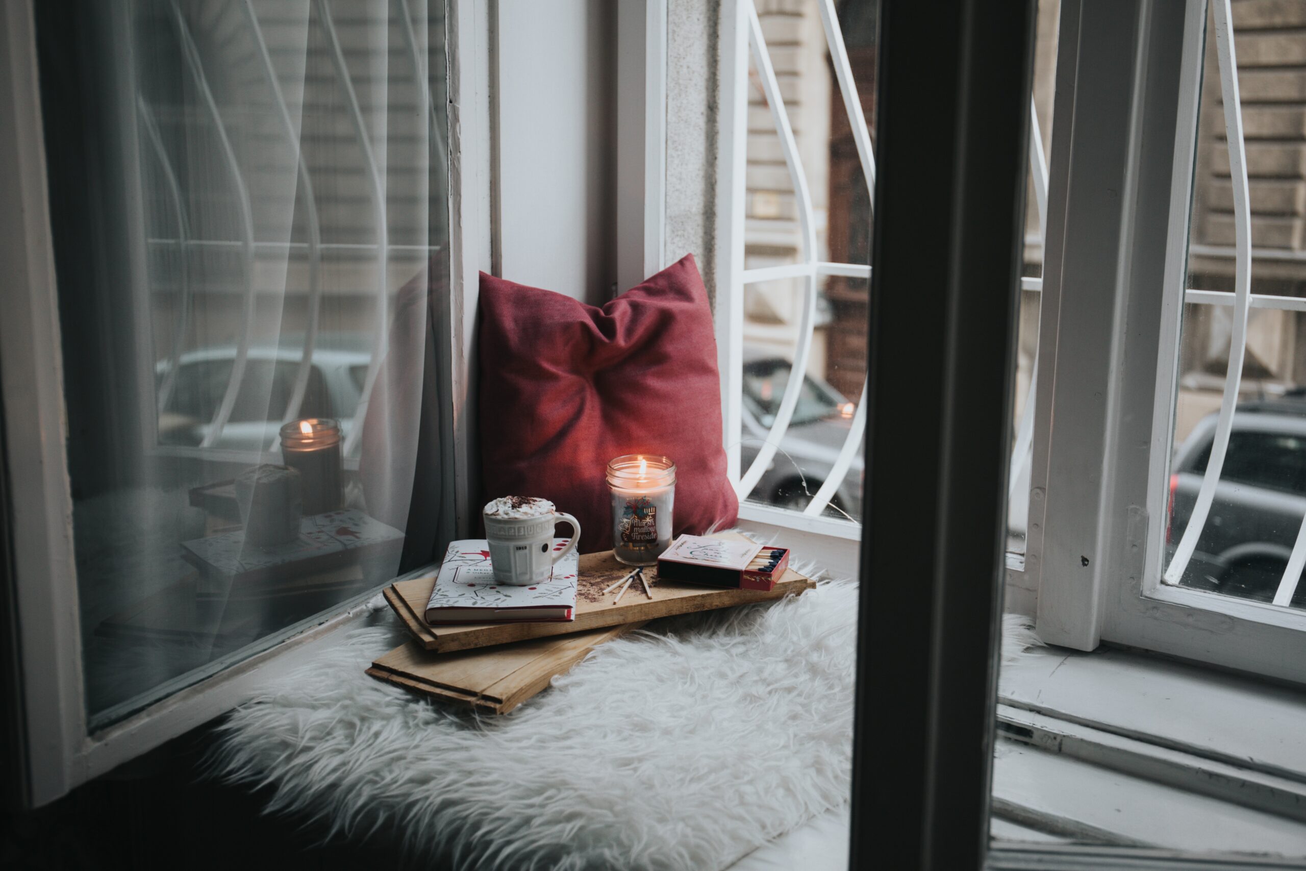 self-care set up by a window, with a pillow, coffee, and books