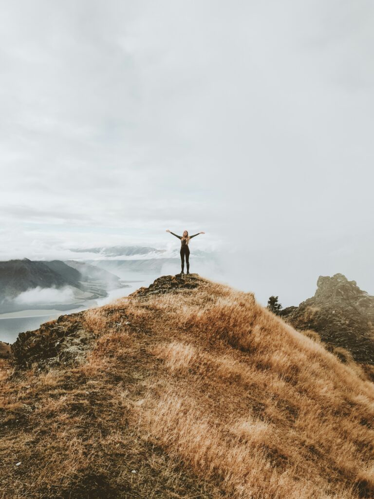 A woman with her arms outstretched, at the top of a hill near the sea. She looks highly motivated, thanks to the holistic counseling available from Awakened Path in New Jersey.