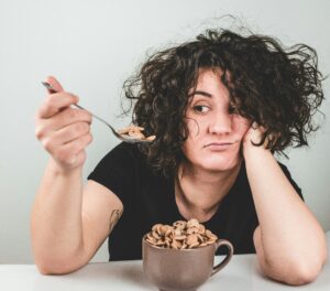 A tired looking woman in New Jersey holding a spoonful of ultra-processed sugar cereal. She is tired of the negative mental health impacts of supposedly health ultra-processed food. 