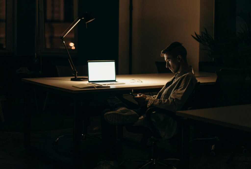 A man is working far into the night because he prioritizes busyness over his mental health. He would benefit from working with Awakened Path to find better work-life integration.