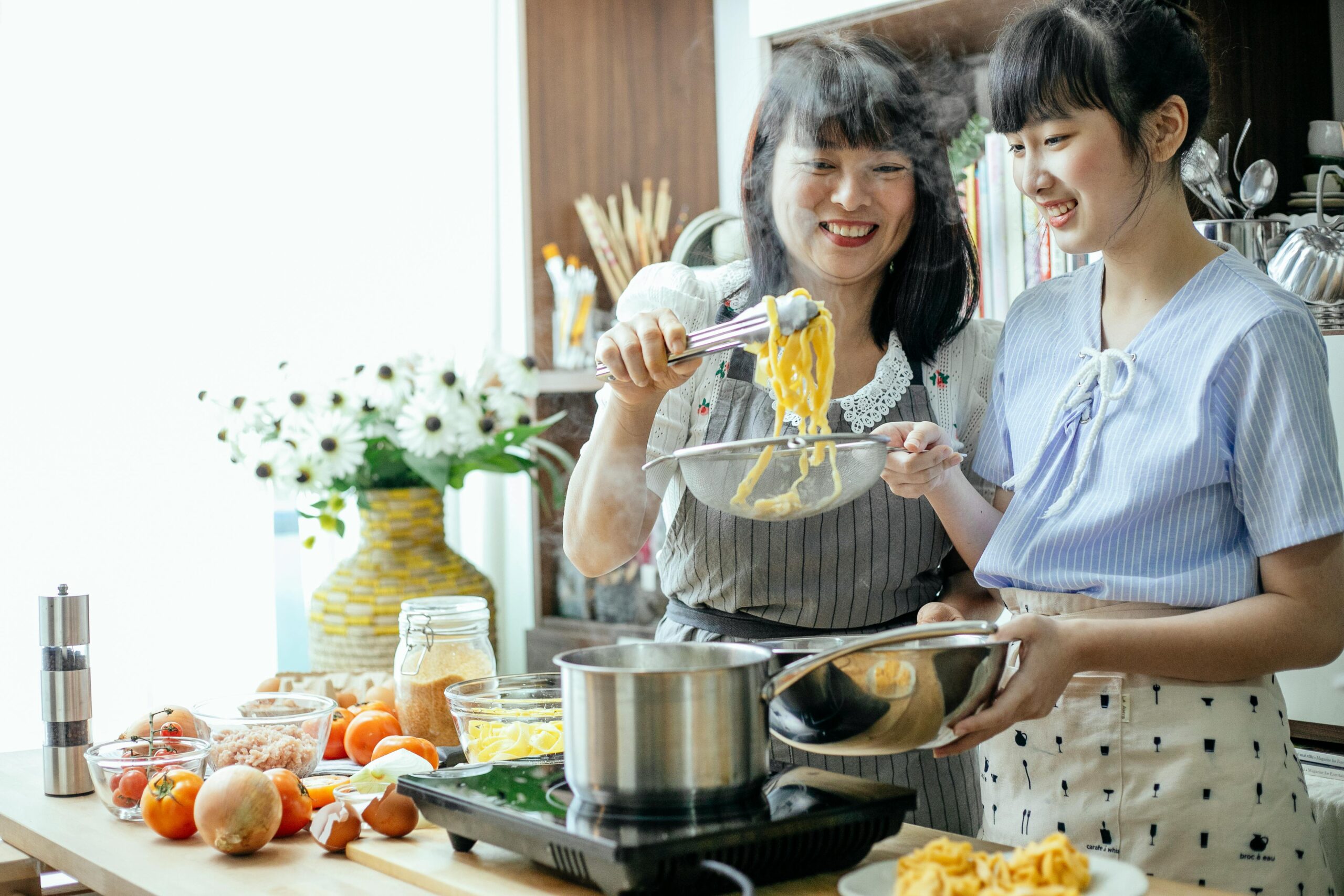 An Asian American mother and teen daughter cook pasta together while bonding as a result of humanistic parenting