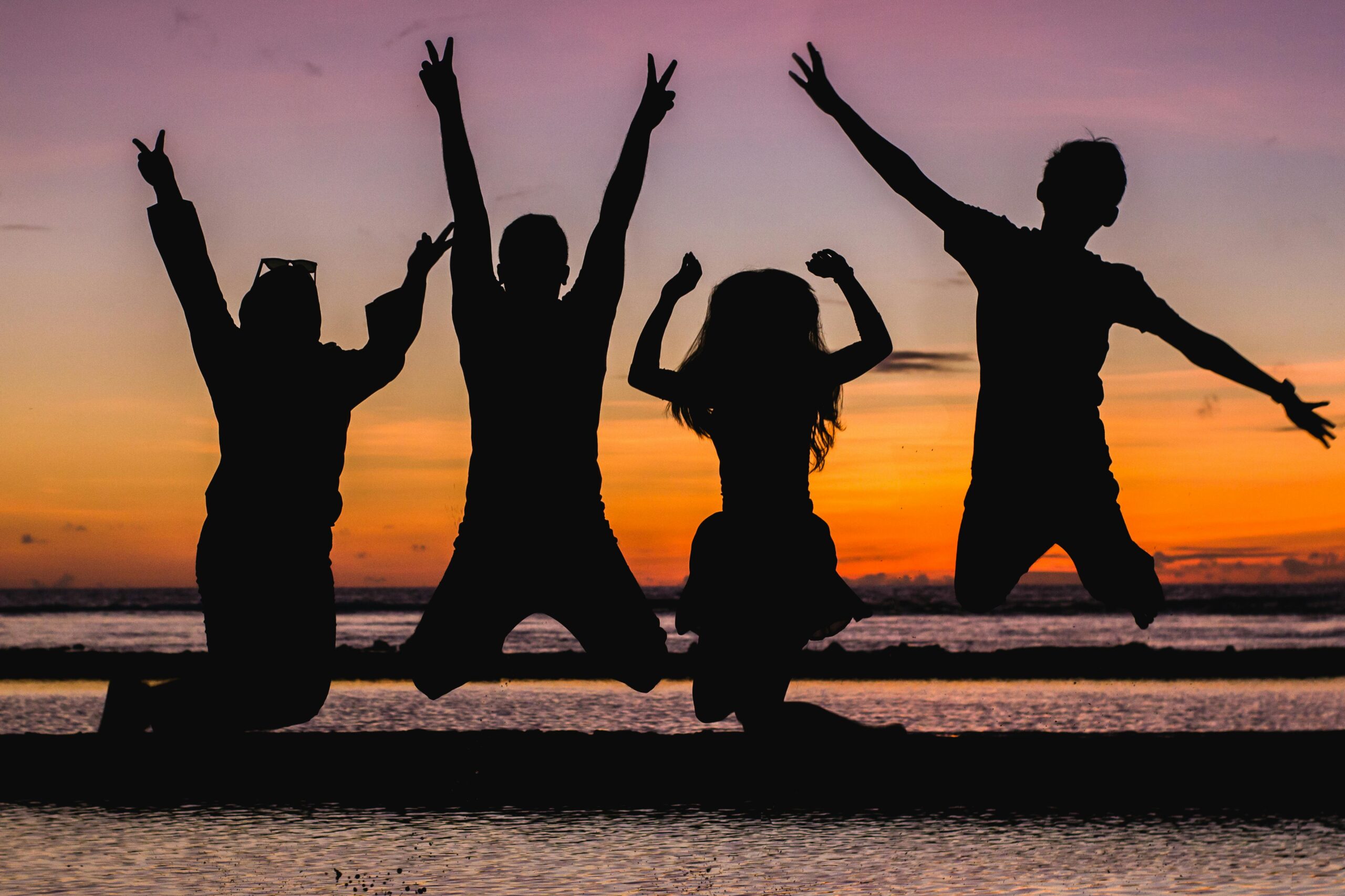 teens jumping on the beach in front of sunset in happiness that their lgbt identities are accepted