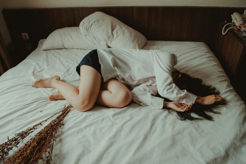Person lying curled on a bed with their face turned away, representing the emotional weight of internalized shame and the struggle for self-acceptance.