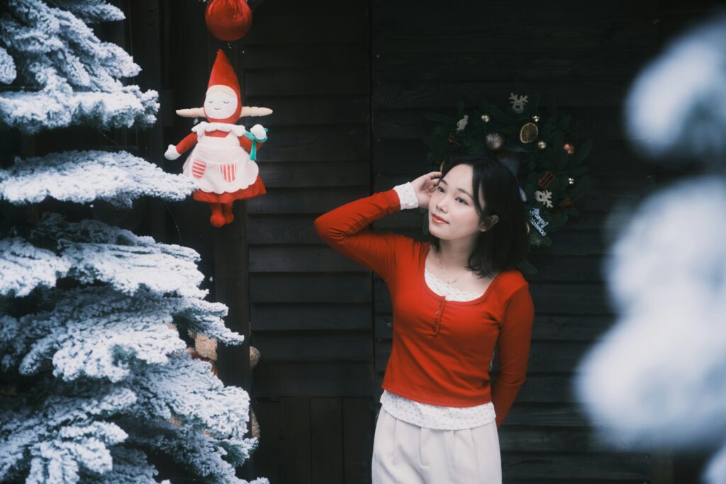 A woman standing beside a snow-covered tree and holiday decorations, appearing thoughtful and reflective during the winter season.
