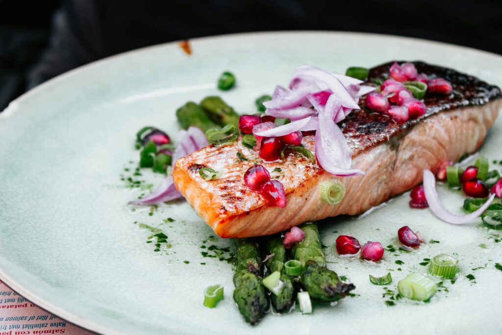 “Grilled salmon served with asparagus, onions, and pomegranate, highlighting omega-3 rich foods that support brain nutrition and reduce anxiety and depression.”