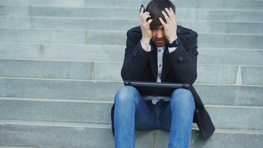 Man sitting on steps with his head in his hands, expressing sadness and frustration associated with grief, loss, and emotional dysregulation when stories end.