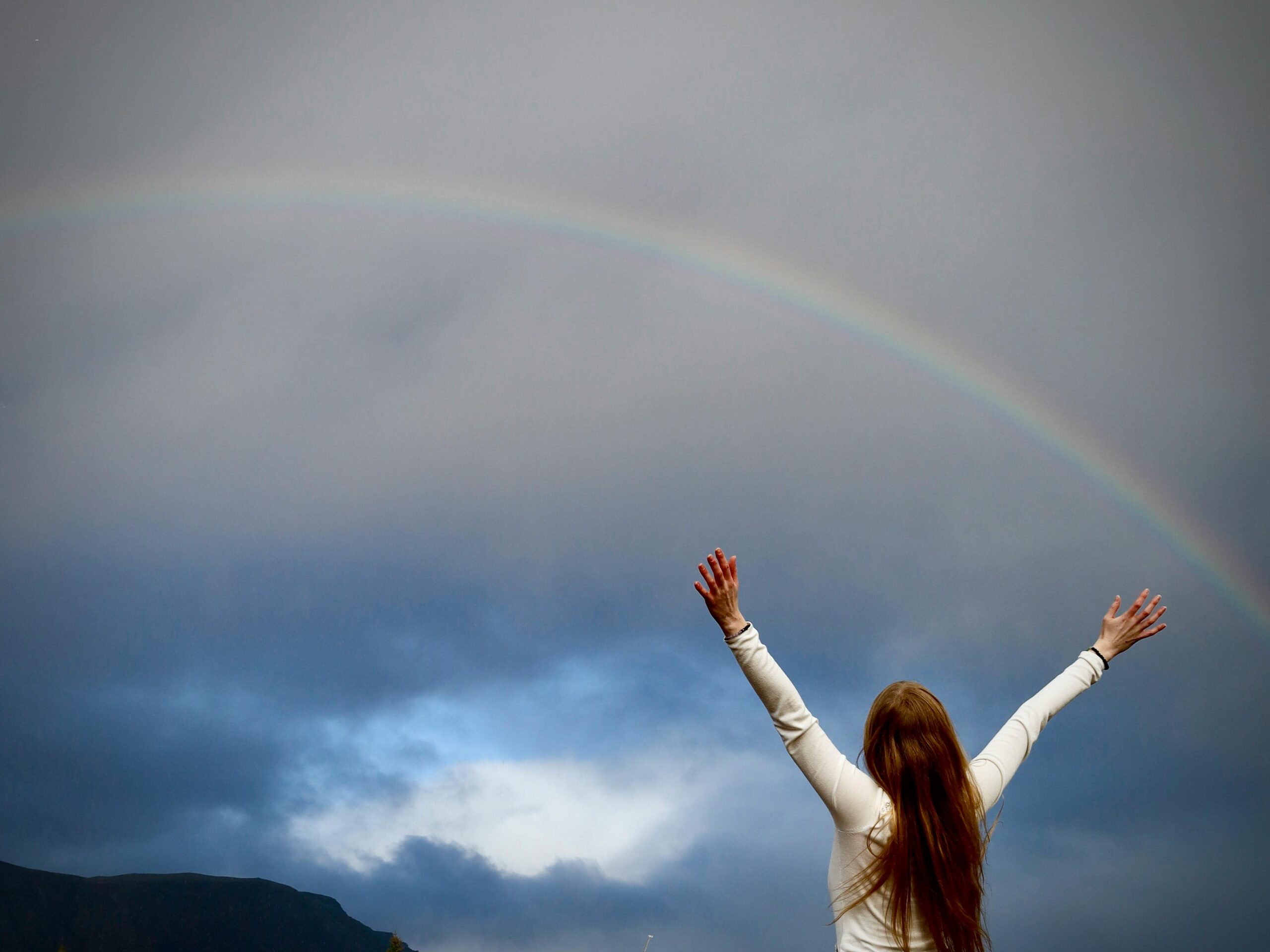Person standing beneath a rainbow with arms raised, symbolizing hope and healing after betrayal trauma and complicated relationship grief.