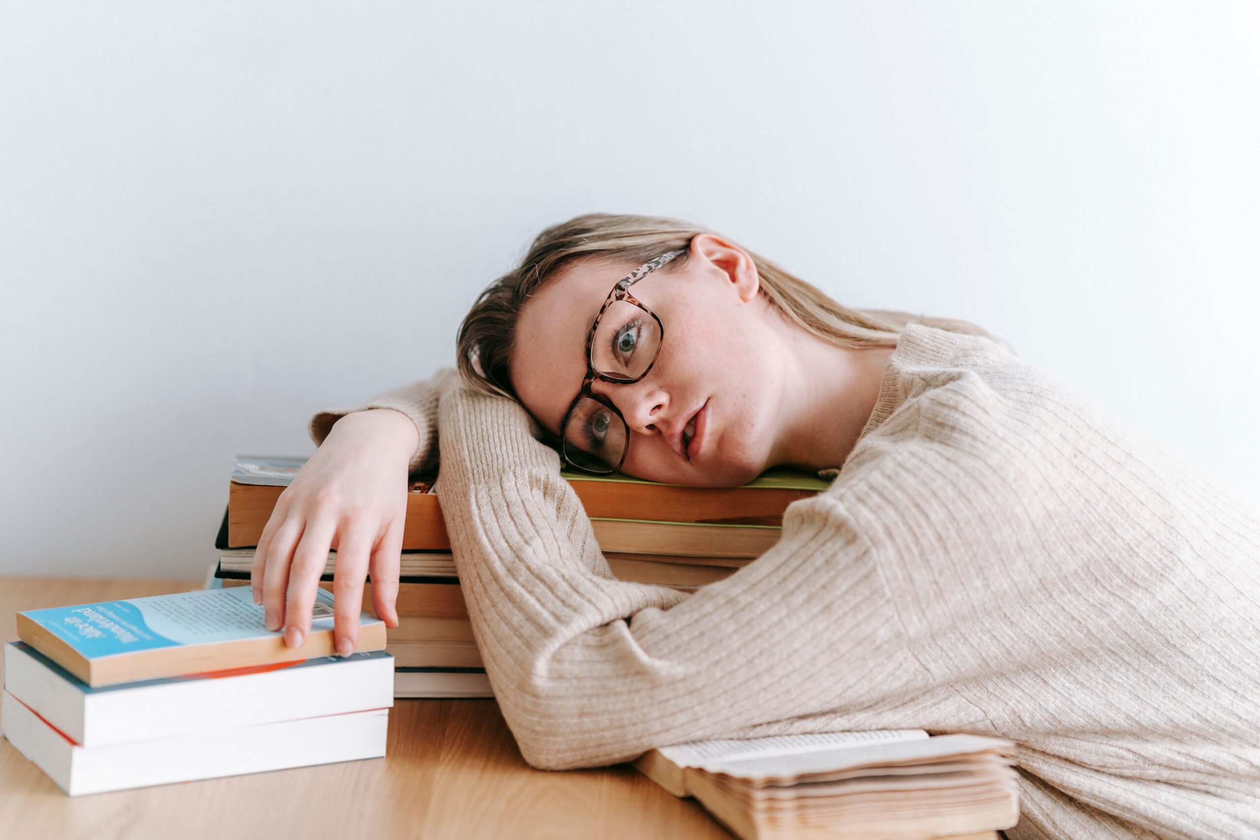 Exhausted woman resting her head on a stack of books as everyday responsibilities feel overwhelming after chronic stress.