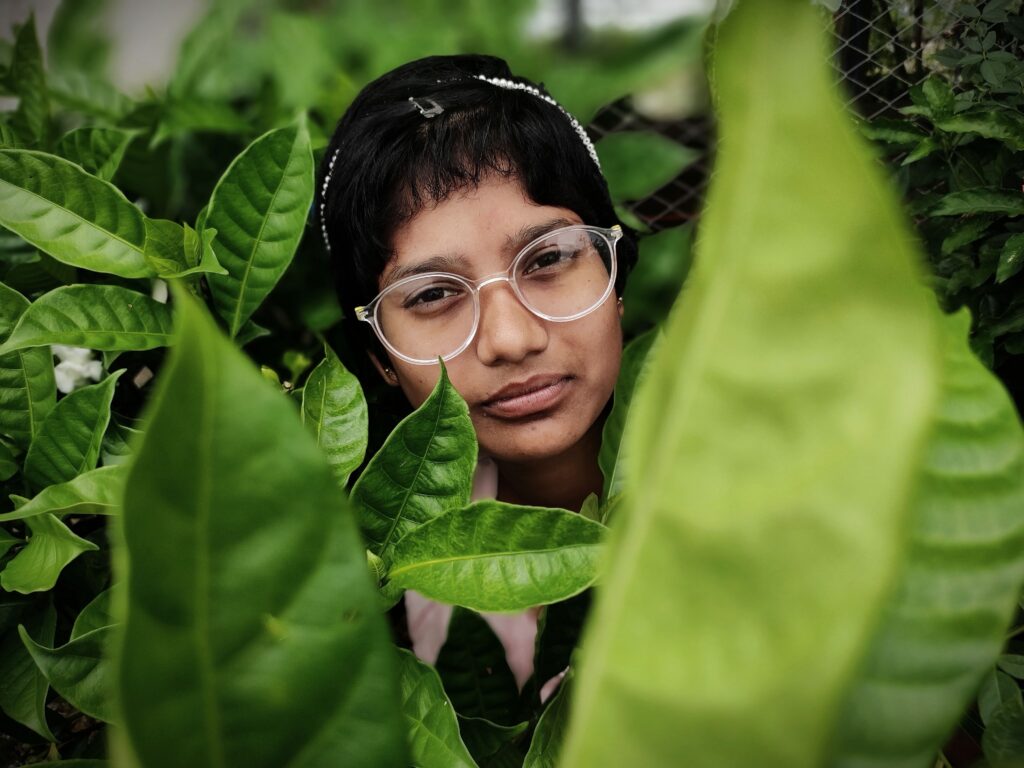 Thoughtful person wearing glasses surrounded by green leaves, reflecting the gradual and nonlinear process of trauma healing.