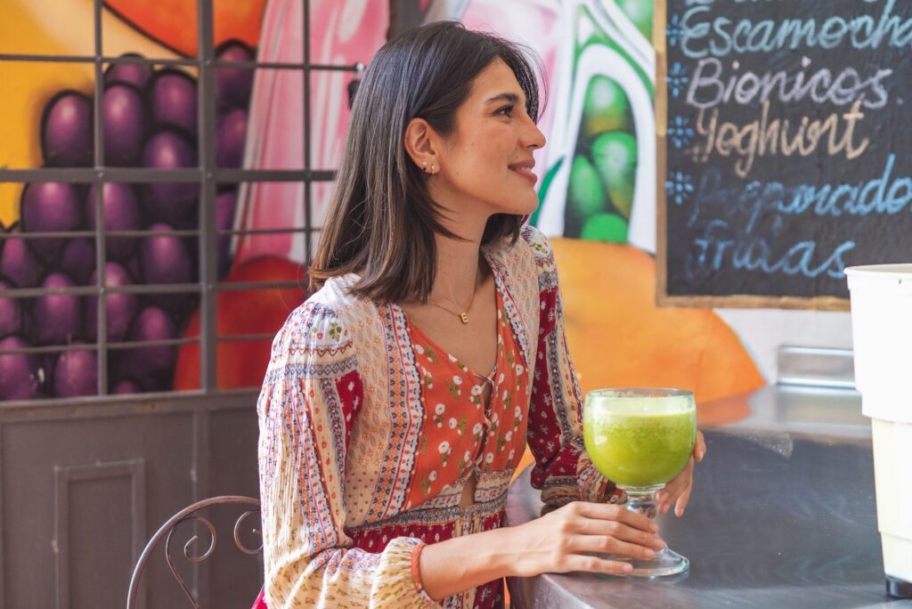 Woman holding a green wellness drink at a café, representing cortisol cocktails, hormone-balancing trends, and holistic stress support.