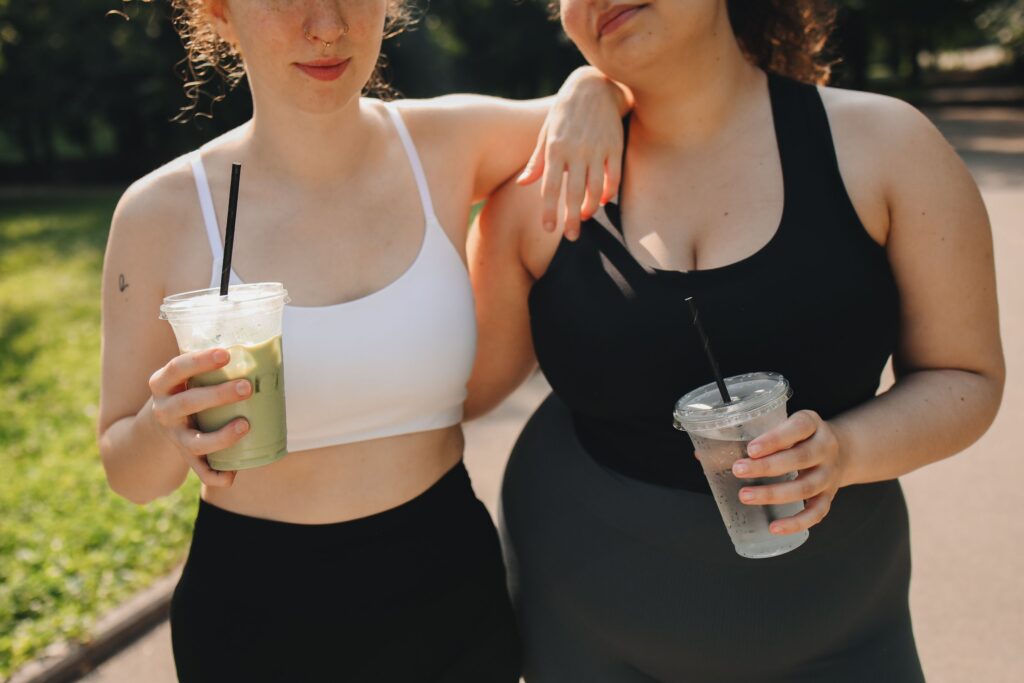 Two women holding drinks after exercise, representing sustainable movement, hydration, and holistic ways to support stress and mental health.